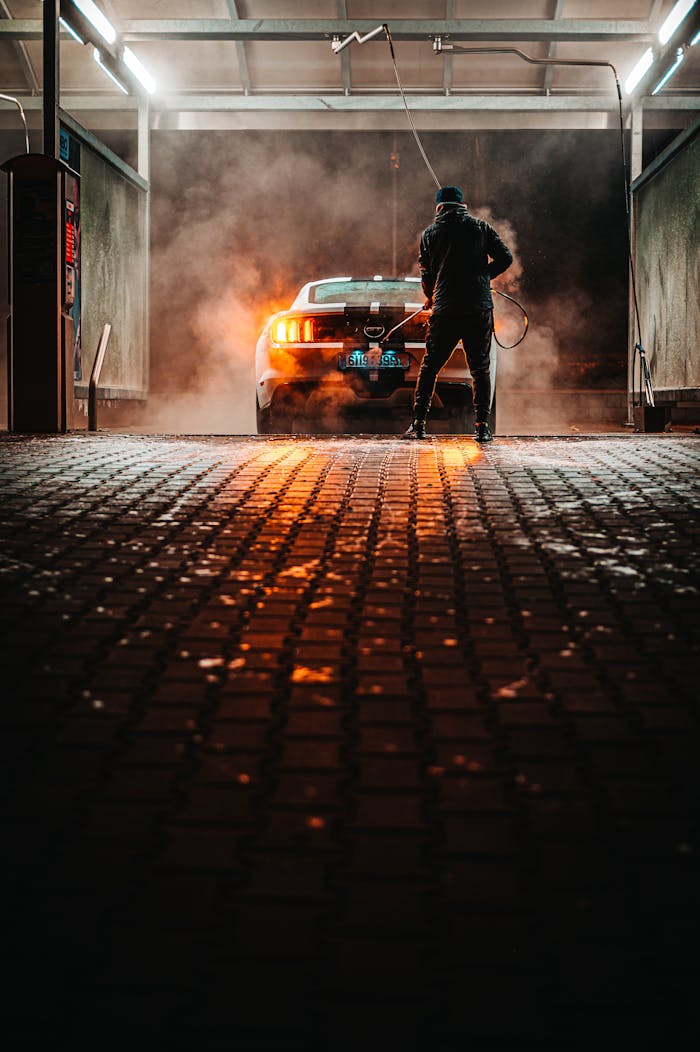A person washing a sports car at a carwash during the night, illuminated by lights.