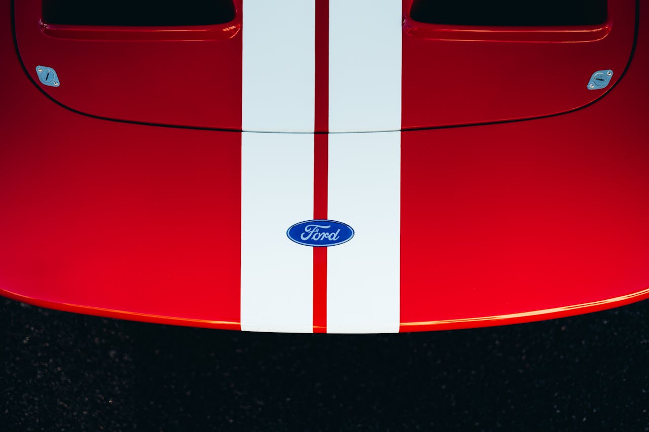 Home Dynamic close-up of a red car hood featuring white racing stripes and Ford emblem.